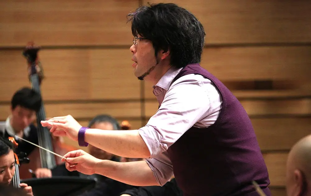 オーケストラの前で指揮棒を振っている指揮者の写真。